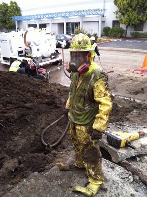 Male in yellow near dirt with big white machinery in background